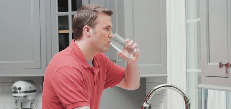 man standing at the sink drinking fresh water from his water filtration system
